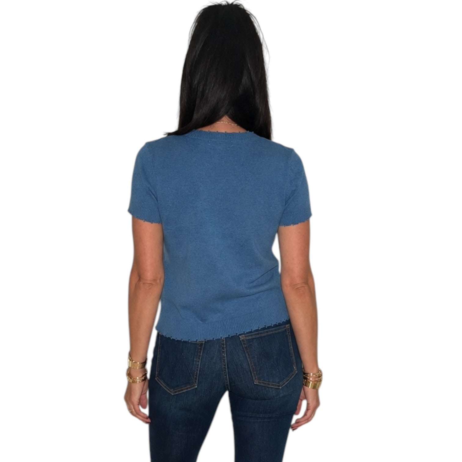 A woman viewed from the back wearing a short-sleeve heathered blue t-shirt and dark blue jeans, set against a plain white background.