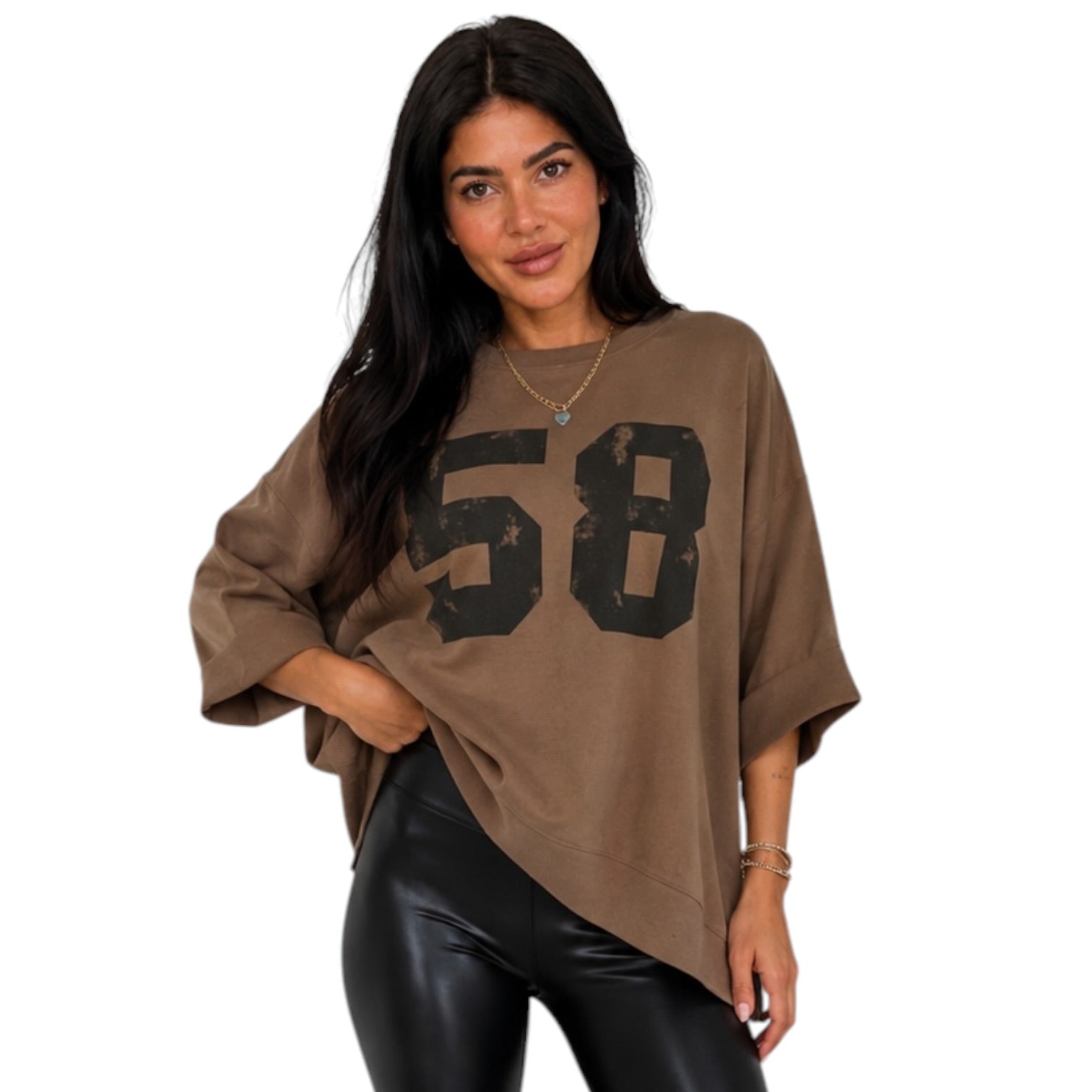 A woman modeling an oversized brown tunic top with a distressed black '58' graphic on the front, paired with black faux-leather pants, against a plain white background.