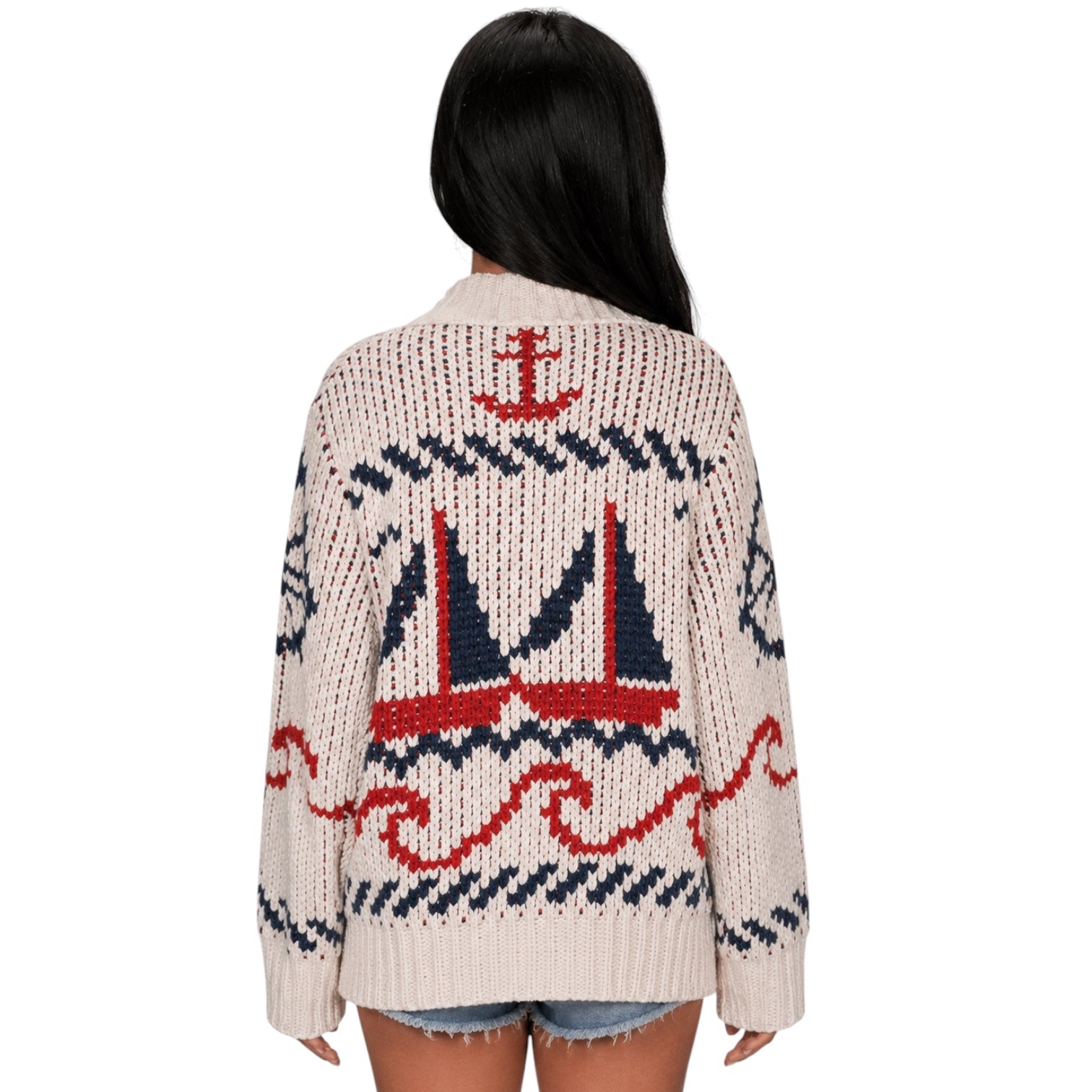 A woman viewed from the back wearing a chunky knit cardigan with a nautical design featuring red and navy blue sailboats and waves on an off-white background.