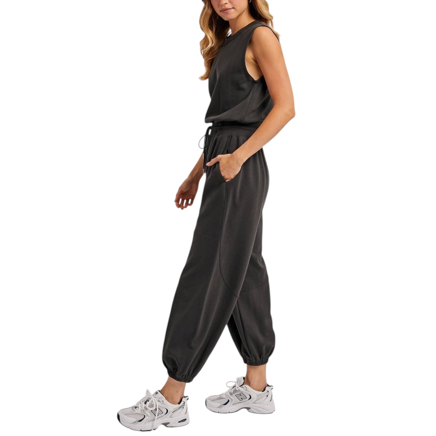 Woman wearing a dark grey jumpsuit with white sneakers on a white background