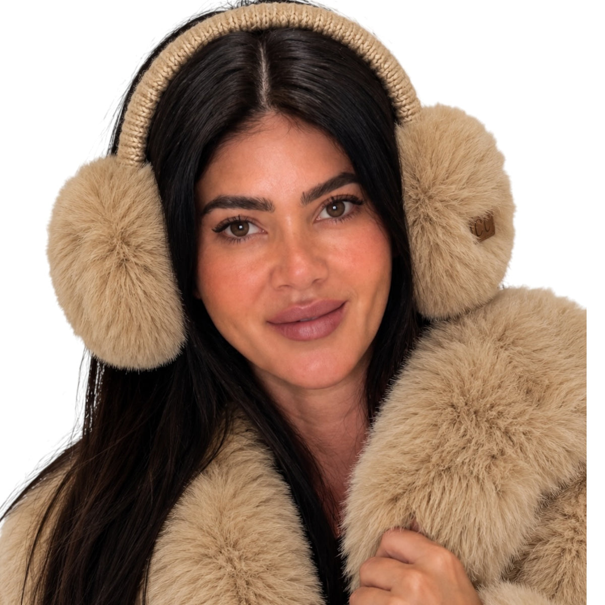 A close-up of a woman wearing beige faux-fur earmuffs with a matching knit headband and a matching beige faux-fur coat, set against a solid white background.
