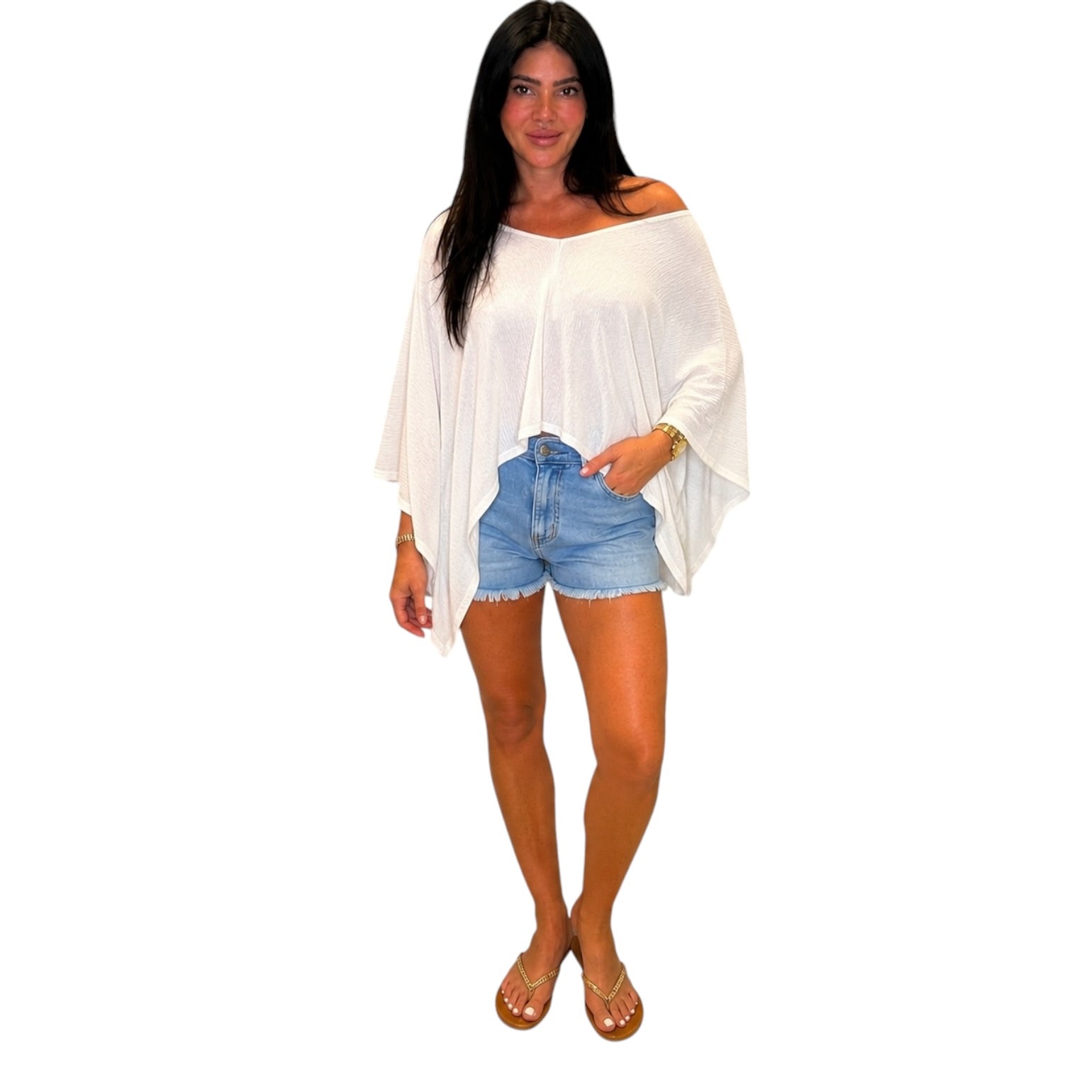 A woman modeling a white off-the-shoulder long-sleeve top paired with light blue denim shorts and brown sandals, set against a plain white background.