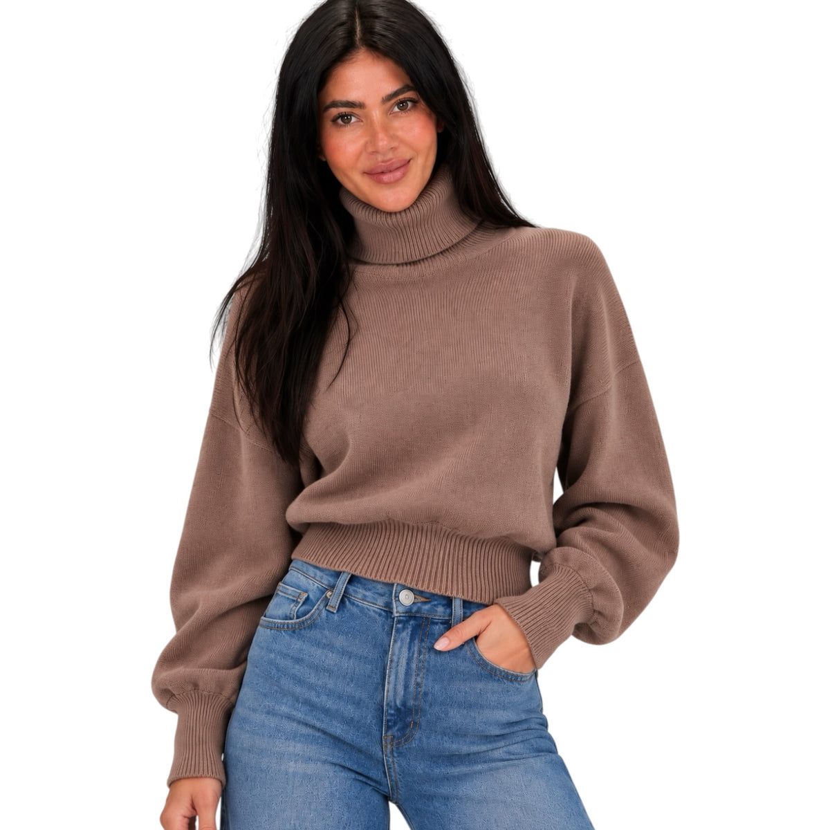 A woman wearing a brown ribbed turtleneck sweater and blue jeans, standing against a plain white background.