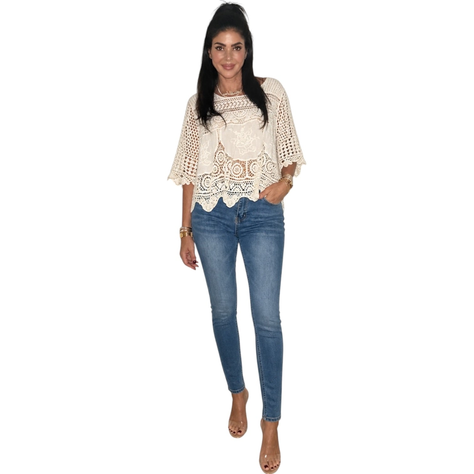 Person wearing a beige crochet top and blue jeans on a white background