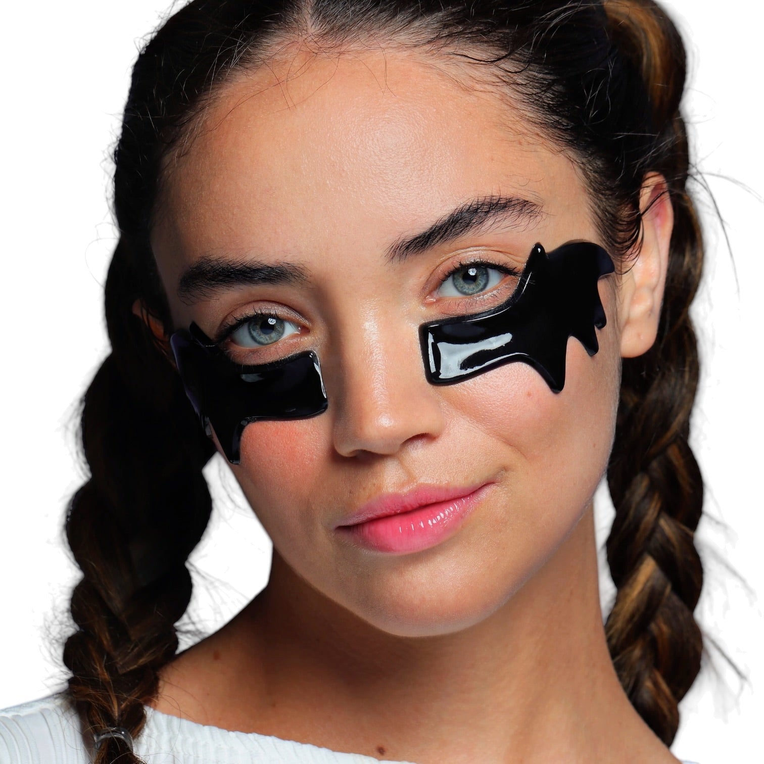 A close-up of a woman with two braided pigtails wearing glossy black eye patches under her eyes, set against a plain white background.