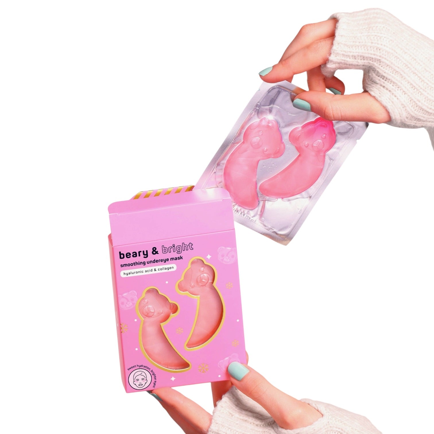 A pink cosmetic mask in a clear plastic blister pack being held above its matching pink retail box by two hands wearing a cream knit sweater. The box reads 'beary & bright smoothing makeup mask'.