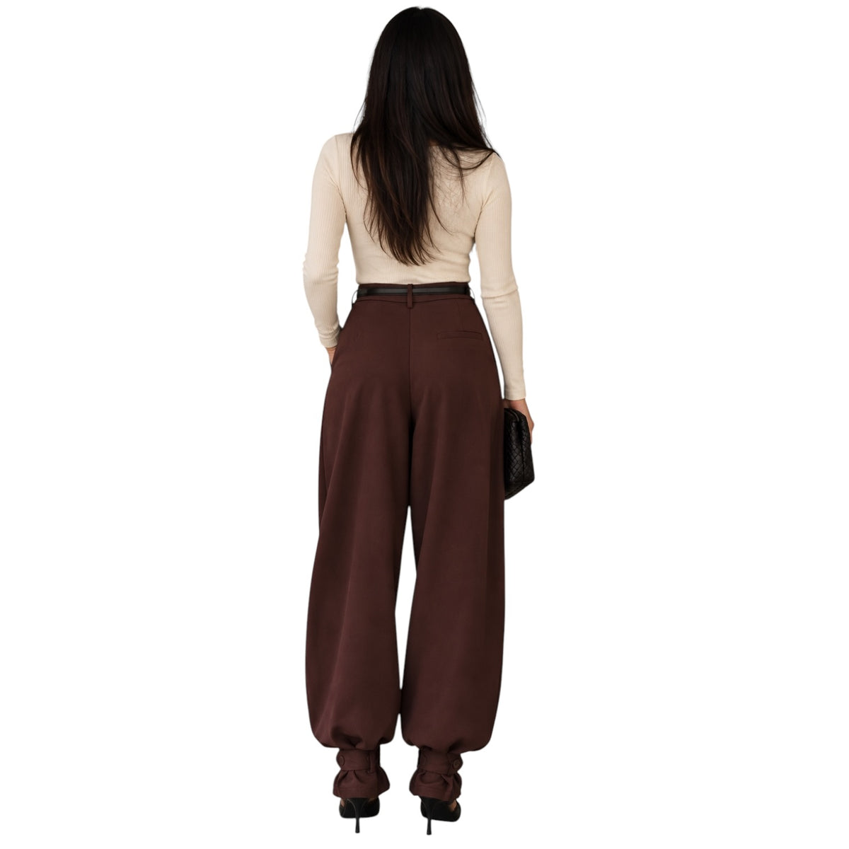 A woman shown from the back wearing high-waisted, wide-leg brown pants, a beige long-sleeve top, and black heels, holding a small black clutch against a plain white background.