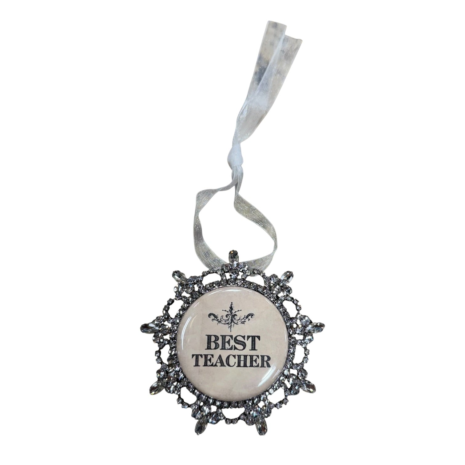 A decorative hanging ornament with a round cream center that reads “BEST TEACHER” in black text, surrounded by an ornate dark silver filigree border and a white ribbon loop at the top.
