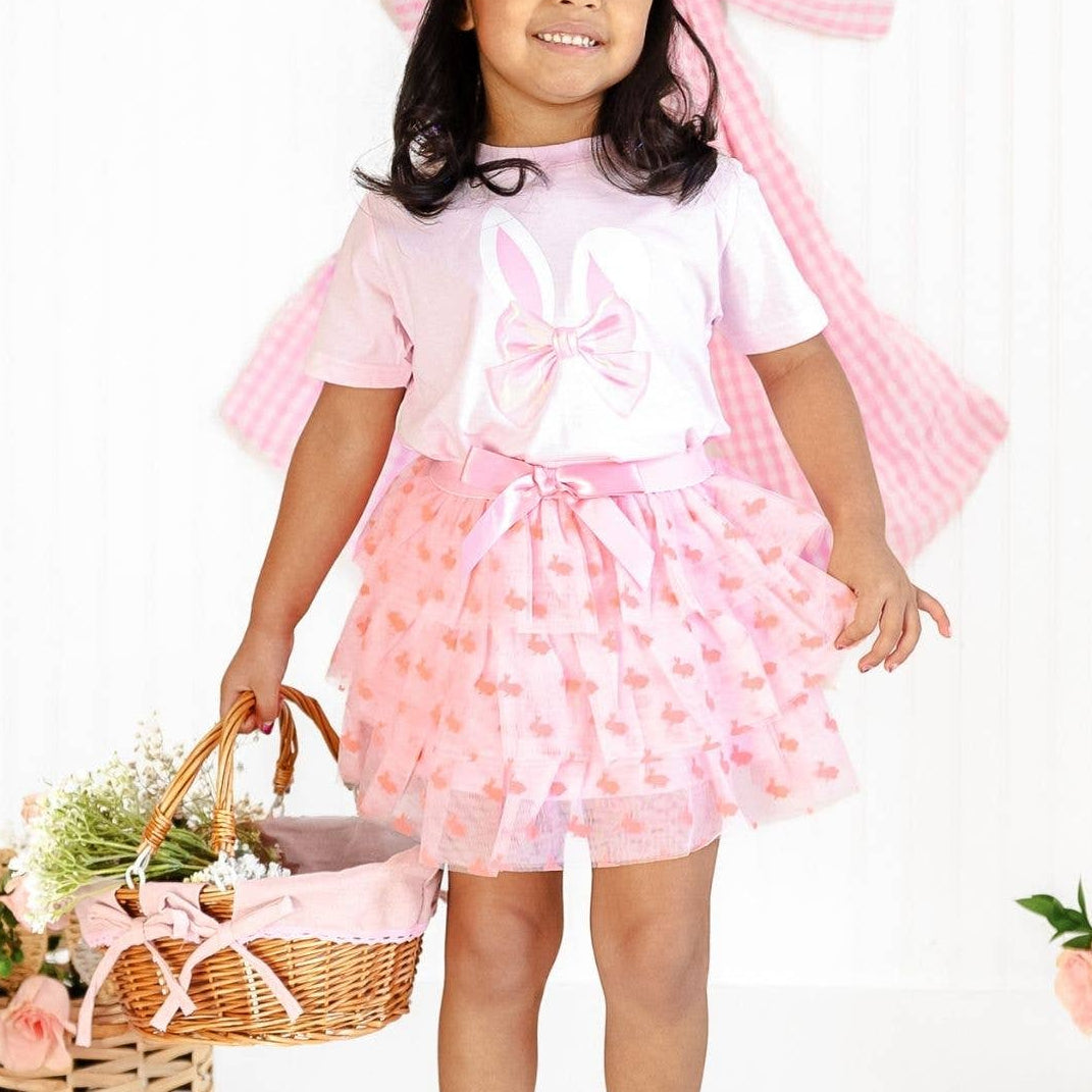 Young girl in a pink outfit with a large bow, holding a basket of flowers on a white background