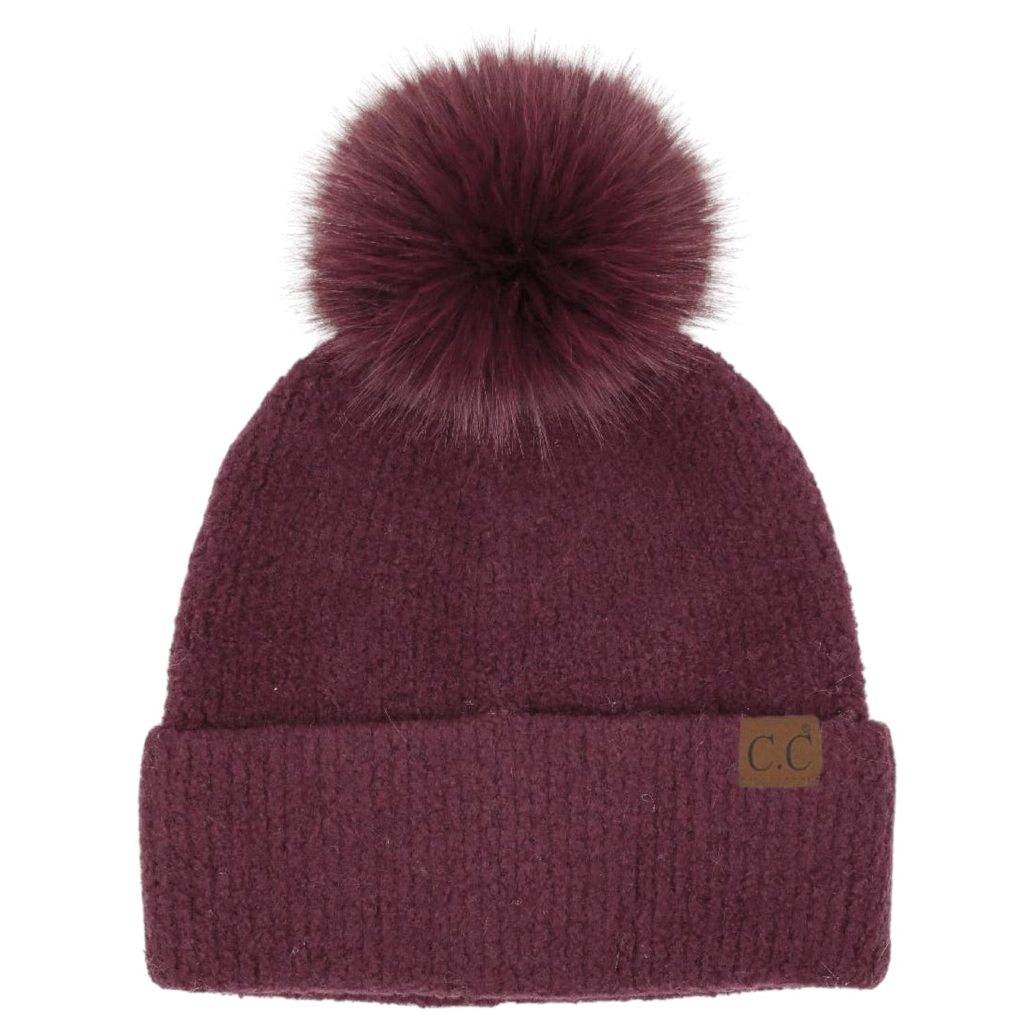 A dark burgundy knit beanie with a large matching faux fur pom-pom on top and a small brown leather 'CC' logo patch on the front cuff, shown against a plain white background.