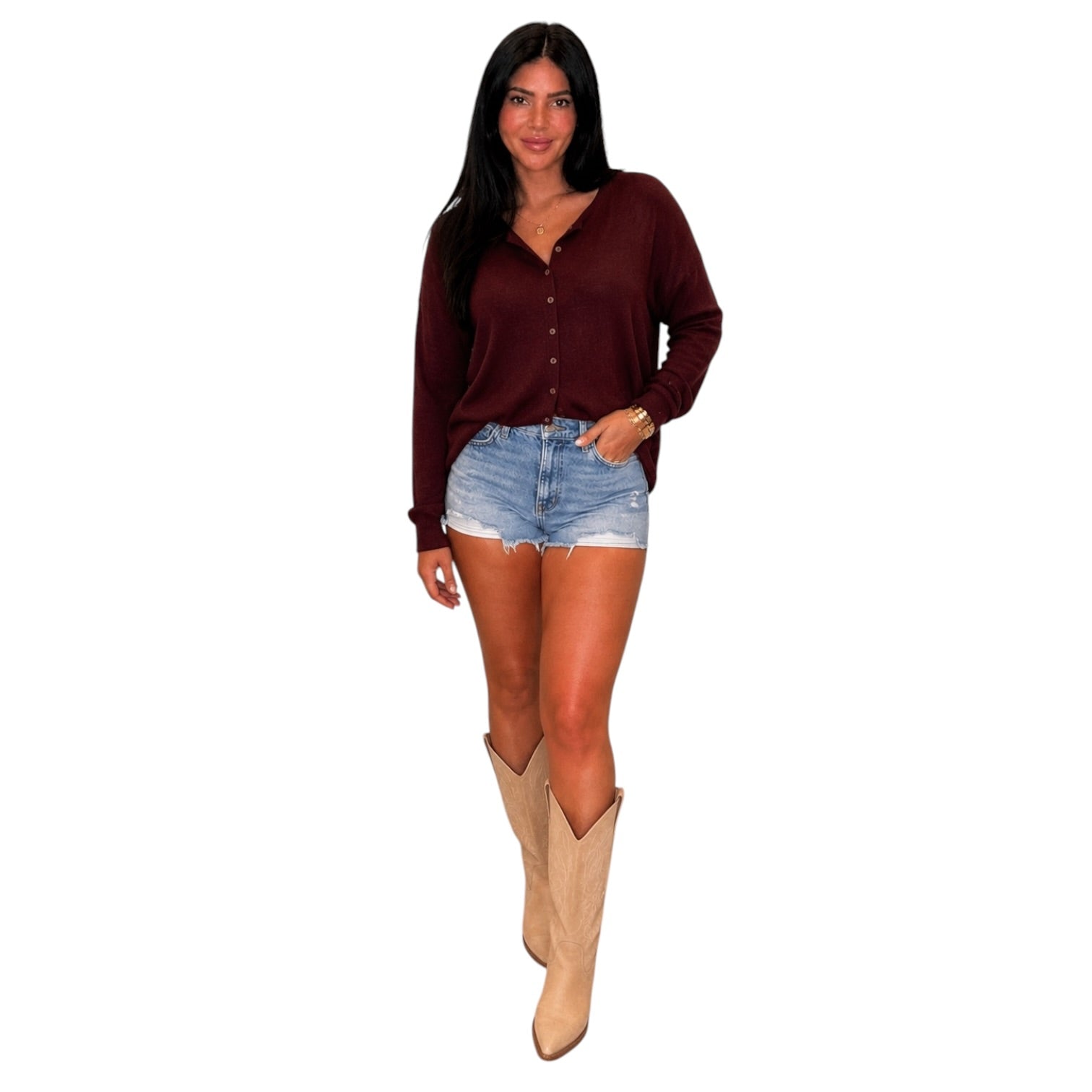 A woman modeling a long-sleeve burgundy button-up top, paired with denim shorts and beige cowboy boots, against a plain white background.