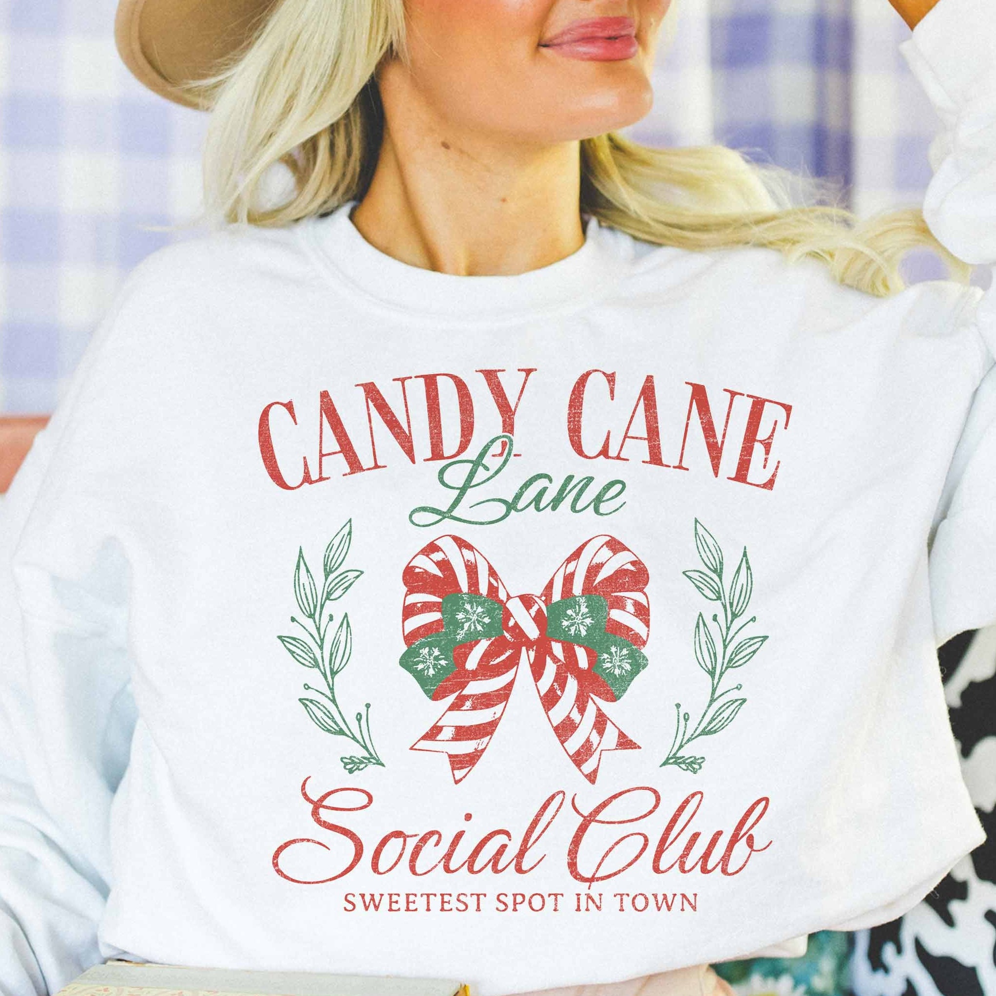 Woman wearing a white sweatshirt with 'Candy Cane Lane Social Club' design.