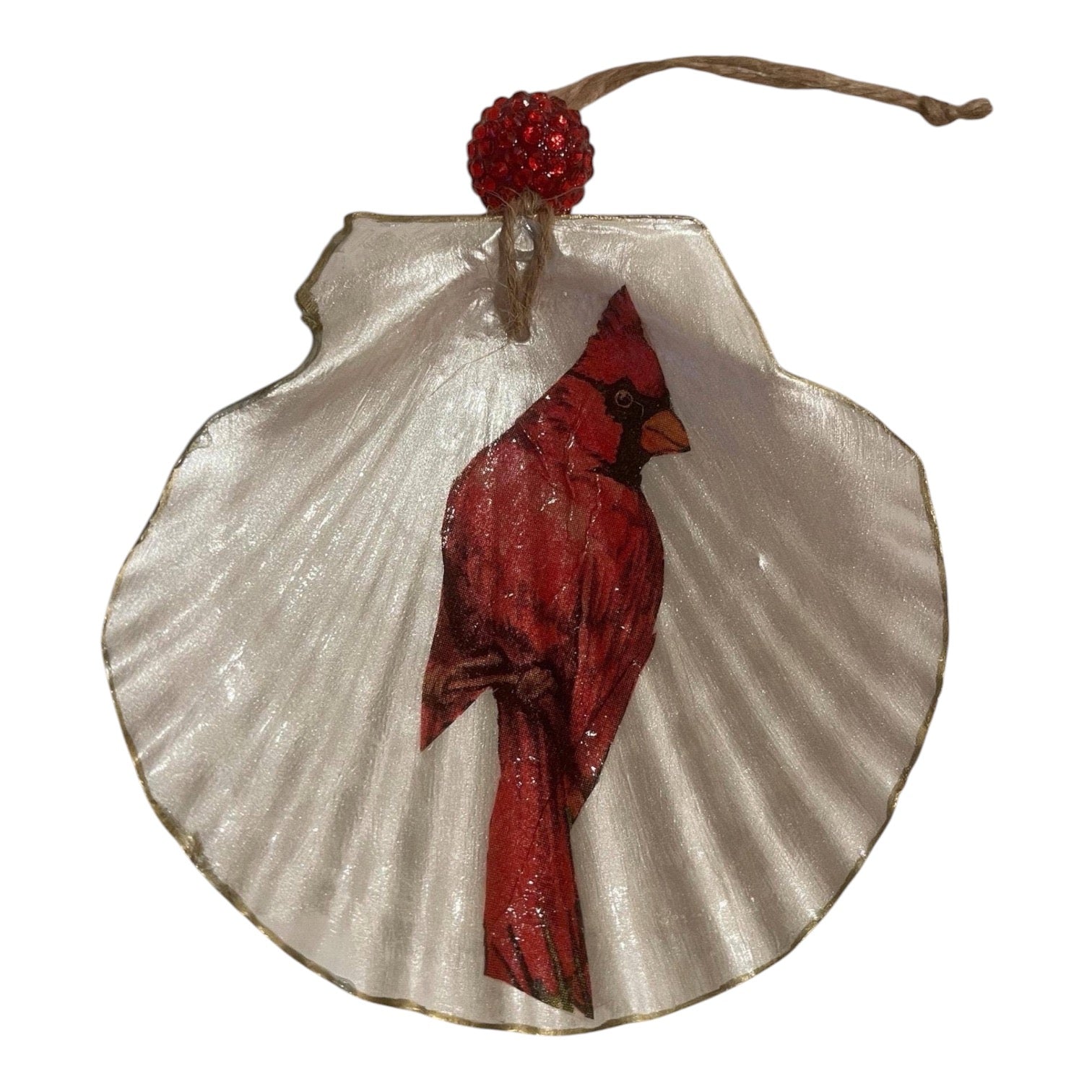 A decorative hanging ornament shaped like a white scallop shell with a red cardinal bird printed or painted across the center, topped with a red beaded loop and natural twine string.