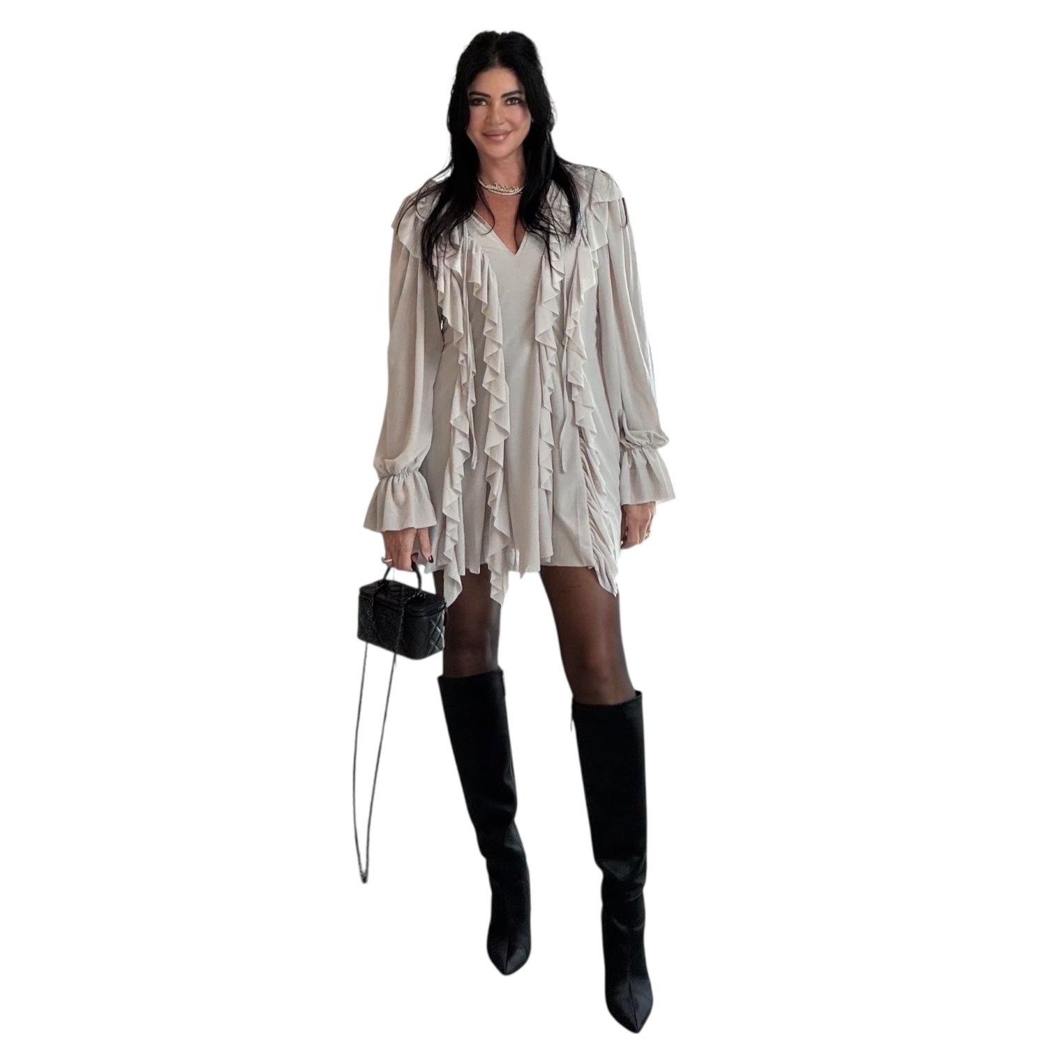 Woman wearing a beige layered romper with black knee-high boots on a white background