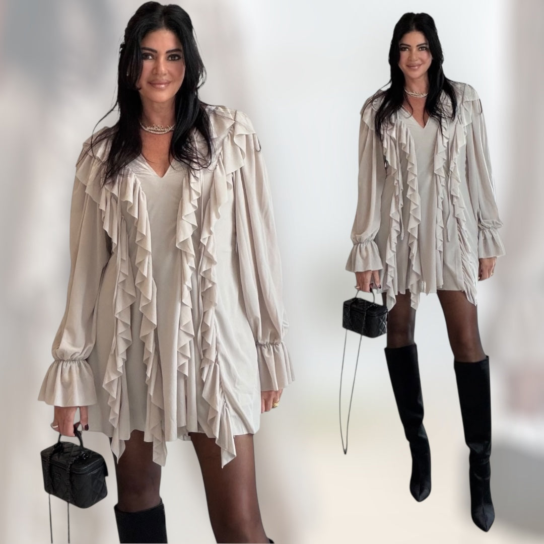 Woman wearing a beige ruffled romper with long sleeves and a V-neckline, holding a black handbag.