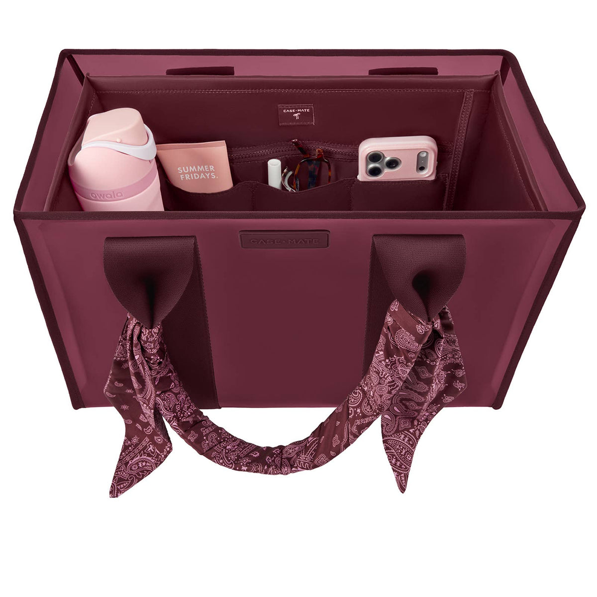 A burgundy tote organizer bag shown from above, filled with travel accessories including a pink tumbler, a phone case, a small box, and a scarf tied to the handles. The brand name 'BAGS & LOVE' is visible on the front and inside the organizer.