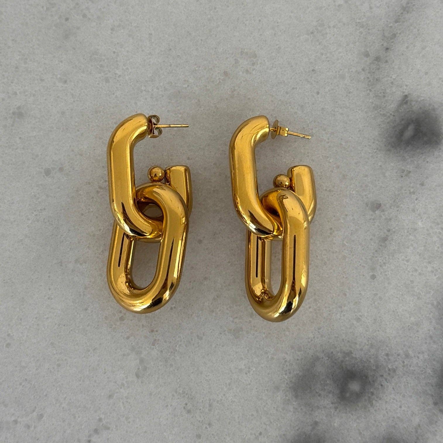 Gold chain-link earrings on a gray concrete surface