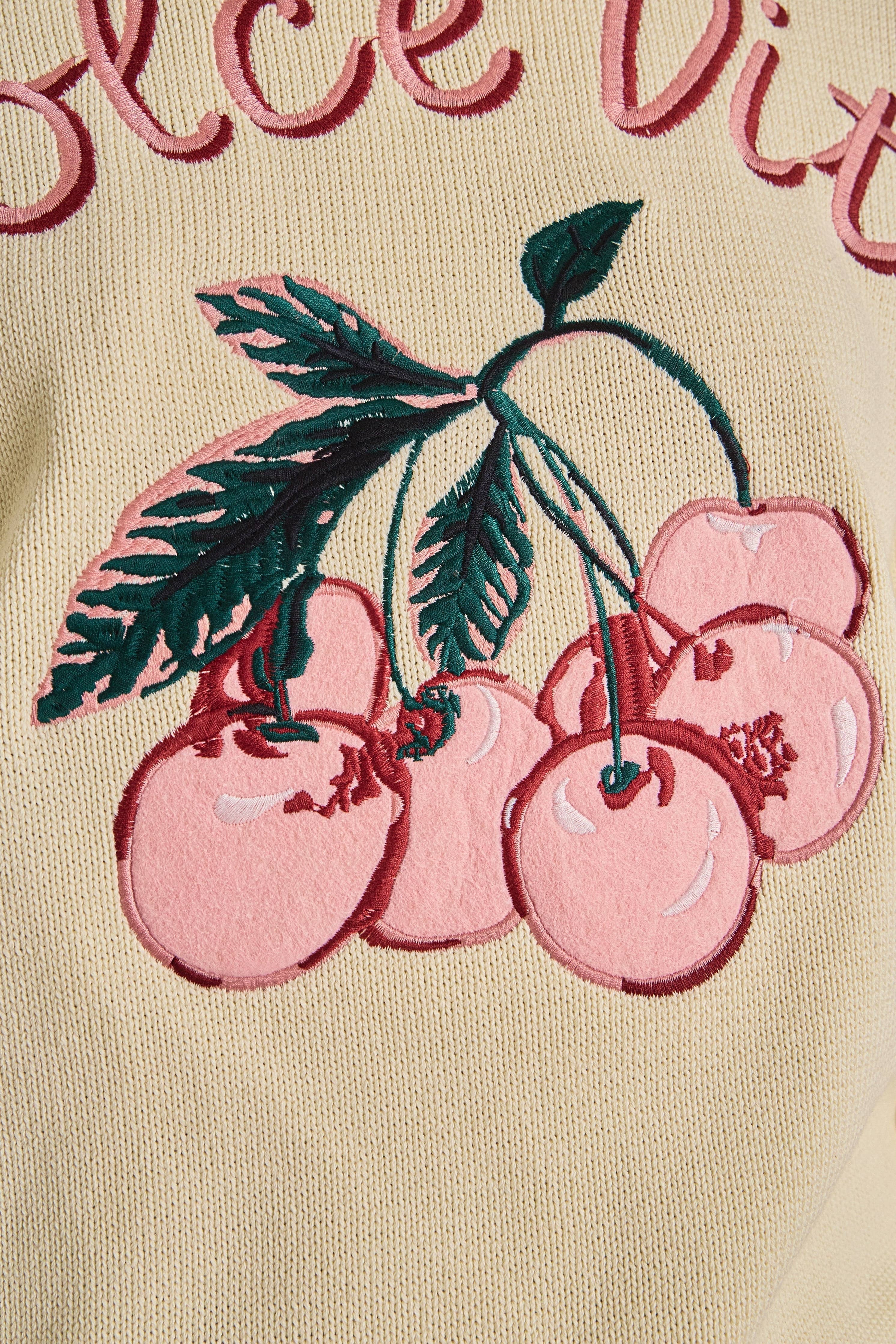 Embroidered pink cherries on a beige background with visible text.