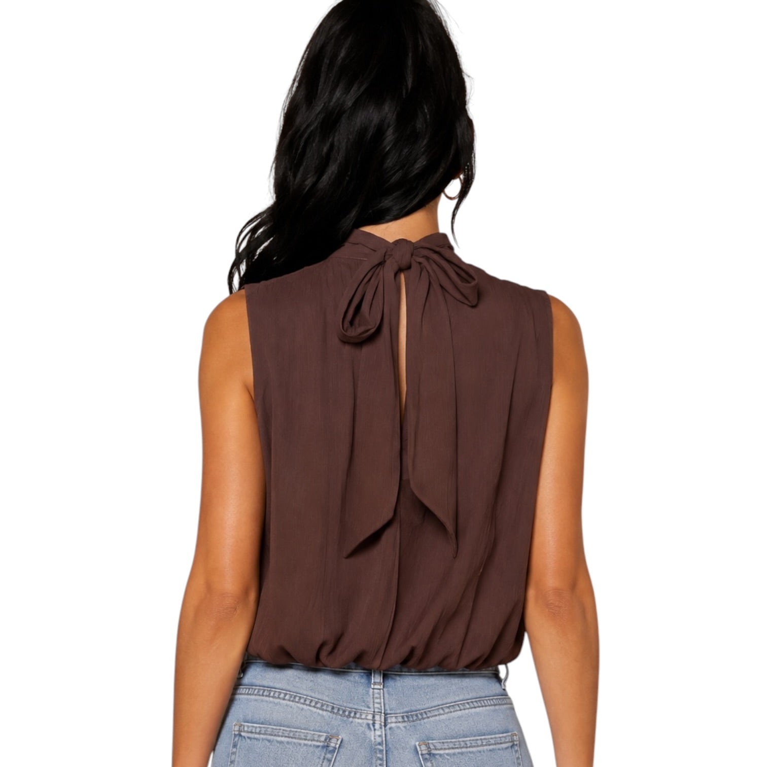 A woman shown from the back wearing a sleeveless brown top with a large bow detail at the back neckline, paired with light blue jeans against a plain white background.