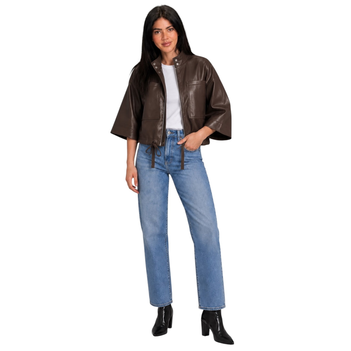 A woman modeling a dark brown cropped faux-leather jacket with wide sleeves, worn over a white t-shirt and blue jeans, on a solid white background.