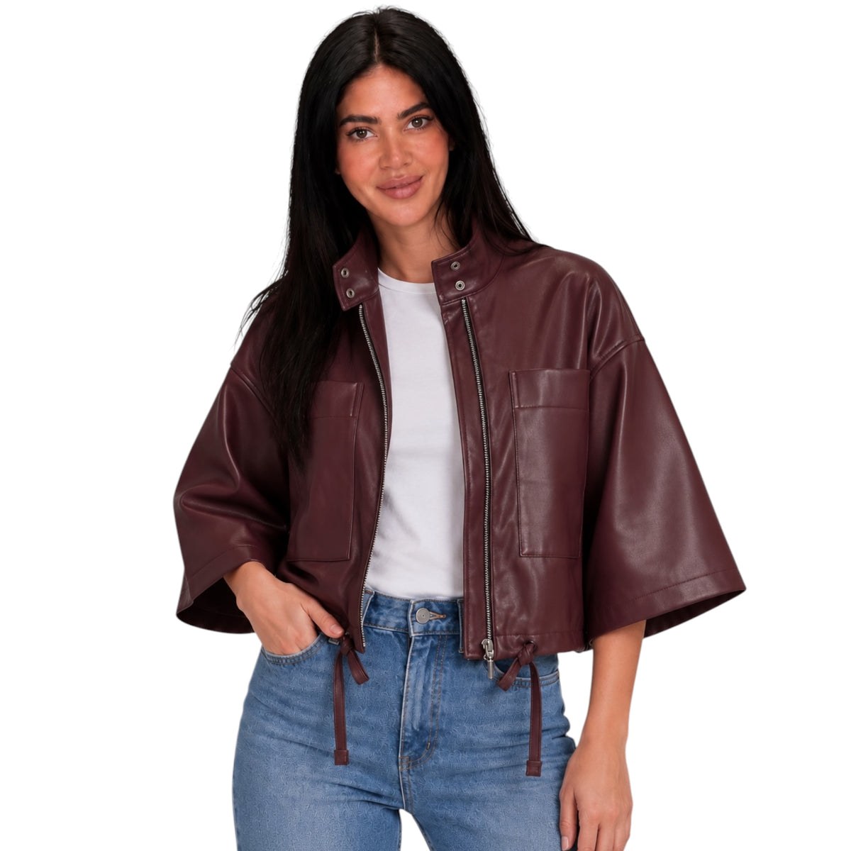 A woman modeling a cropped, wide-sleeved faux leather jacket in a deep burgundy brown color, worn over a white t-shirt and blue jeans against a plain white background.