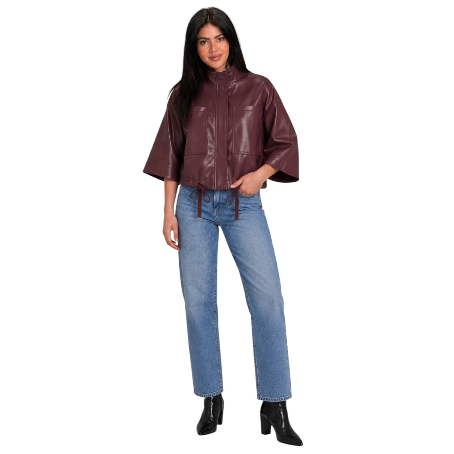 A woman modeling a cropped, short-sleeved faux-leather jacket in a deep burgundy color, paired with blue jeans and black ankle boots, against a plain white background.