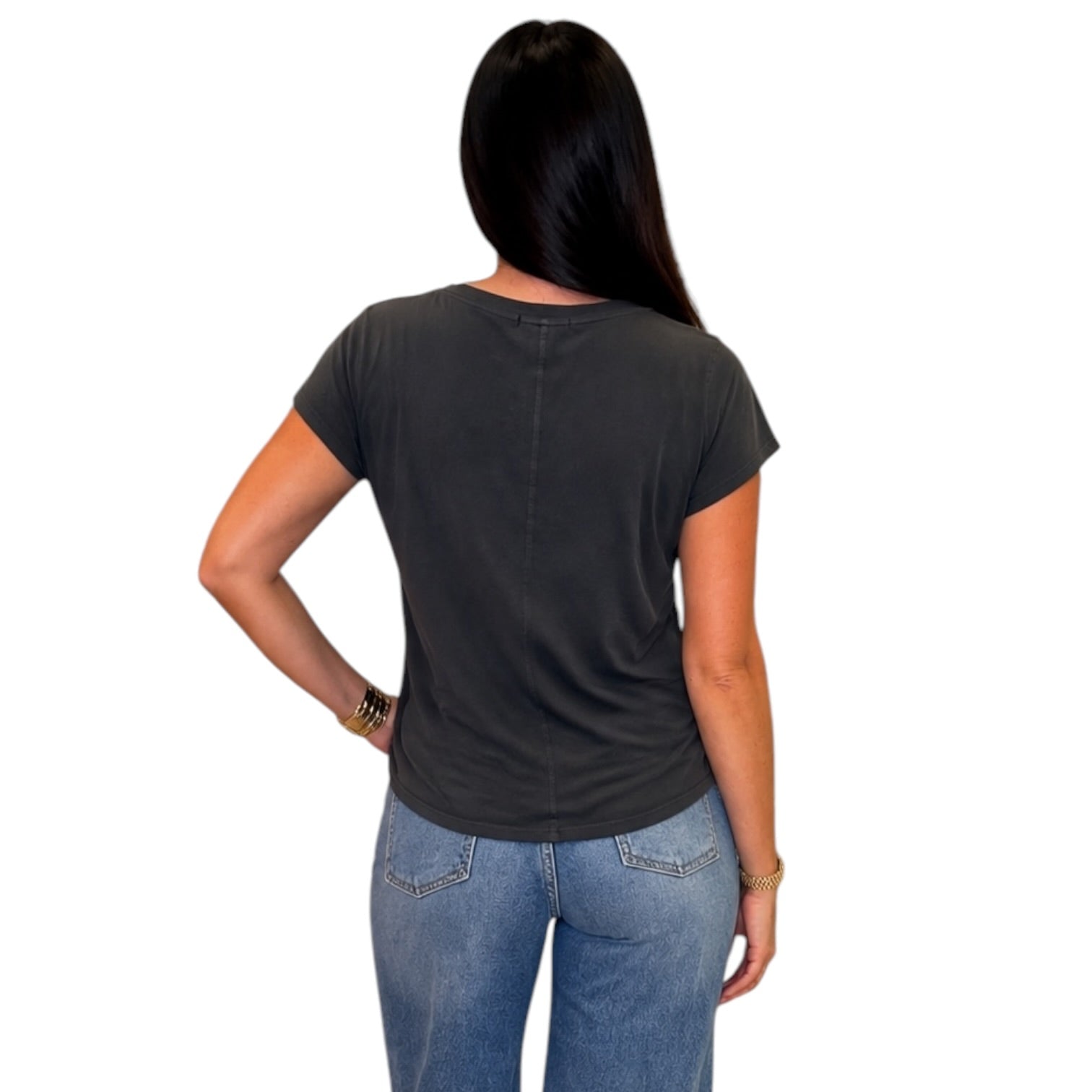 A woman viewed from the back wearing a dark charcoal gray short-sleeve t-shirt and blue jeans, set against a plain white background.