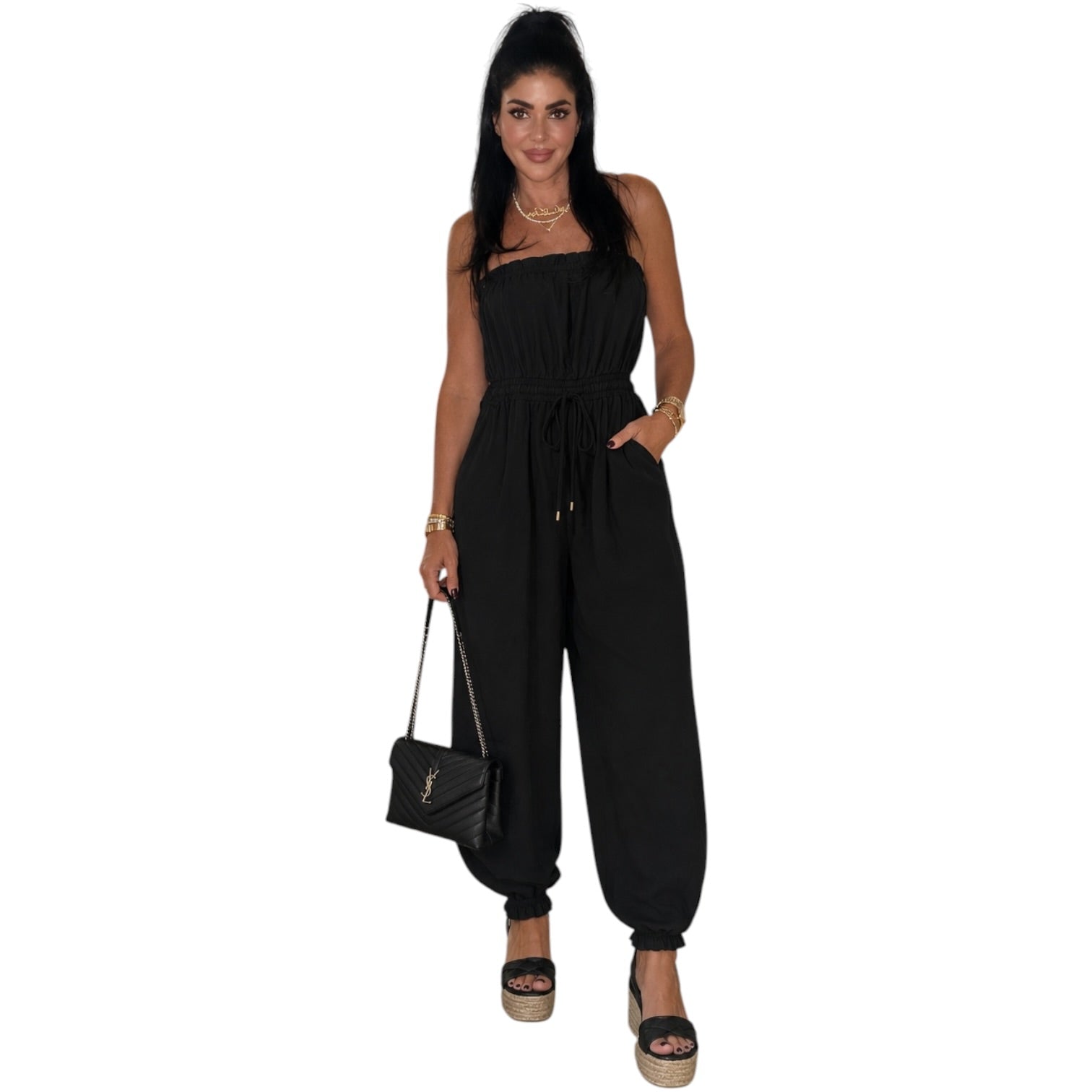 Woman wearing a black jumpsuit holding a black handbag on a white background