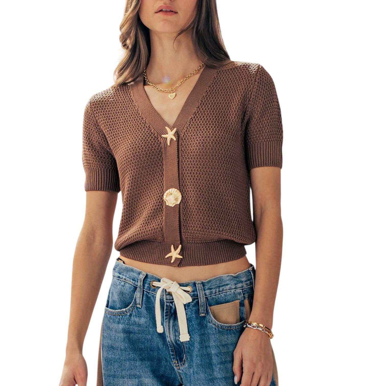 Woman wearing a brown knitted cardigan with starfish buttons and blue jeans on a white background