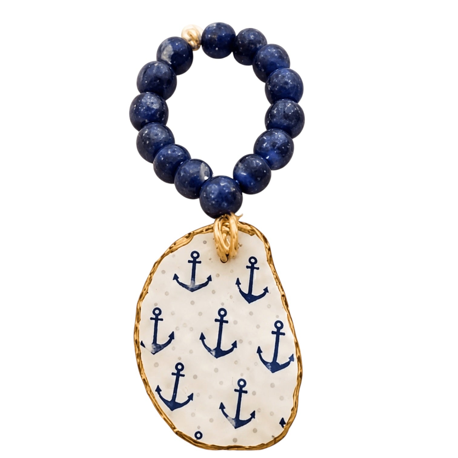 A beaded bracelet with dark blue lapis lazuli stones and a dangling irregular white stone charm decorated with navy blue anchors and gold trim, shown on a plain white background.