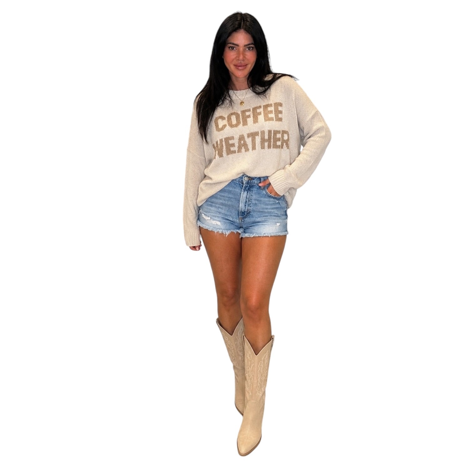 A woman modeling a cream-colored long-sleeve sweatshirt with 'COFFEE WEATHER' printed in brown across the chest, paired with denim shorts and beige cowboy boots, set against a plain white background.