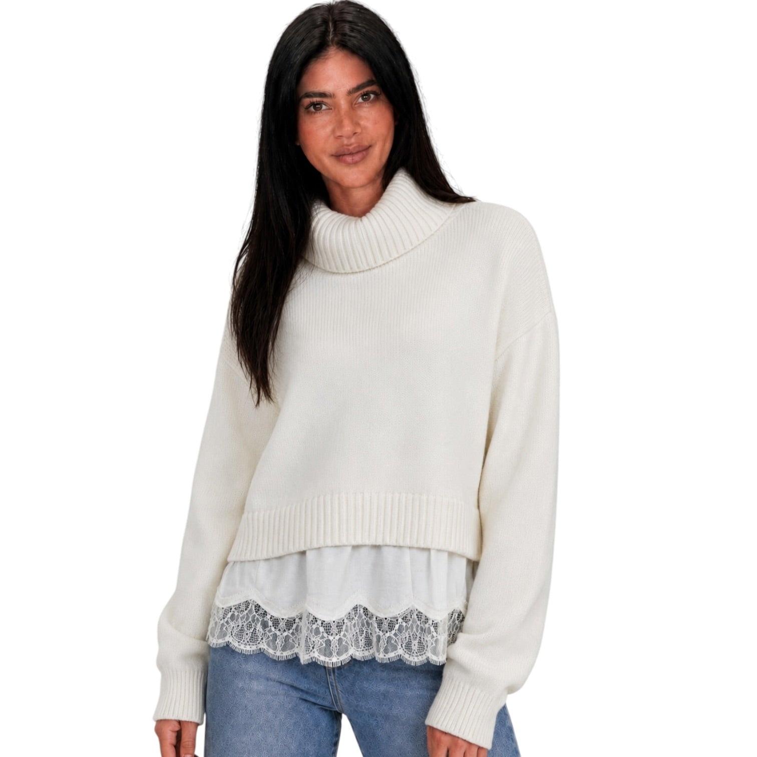 A woman wearing a cream-colored knit turtleneck sweater with a lace hem detail, paired with blue jeans, against a plain white background.