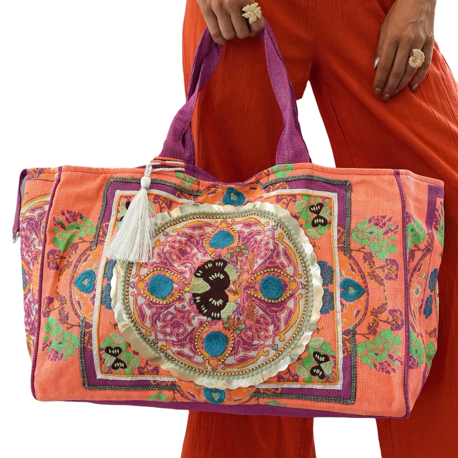Colorful embroidered bag held by a person wearing orange pants on a white background