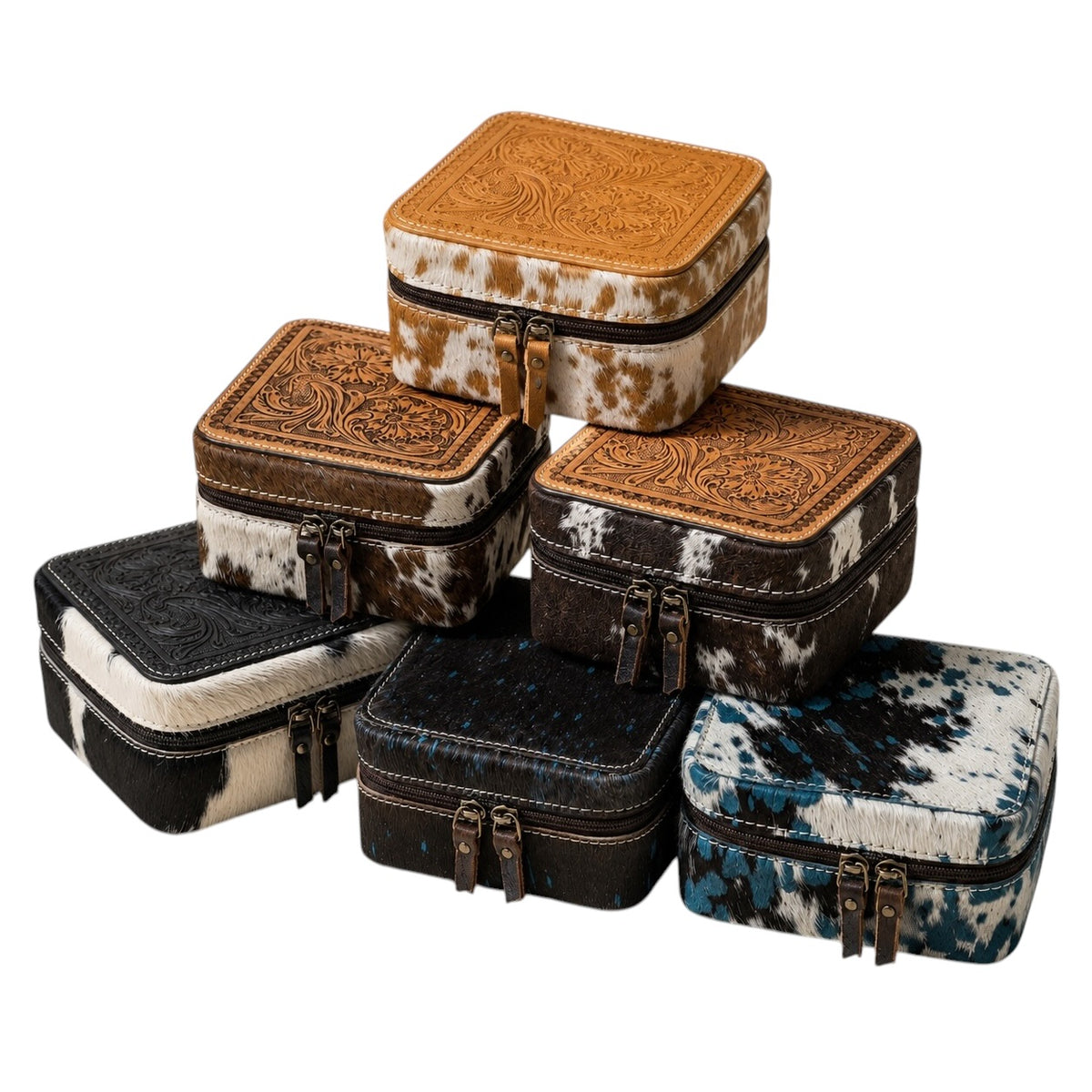 A stack of six western-style jewelry boxes in various cowhide and leather patterns, including tan, brown, black, and blue, set against a plain white background.