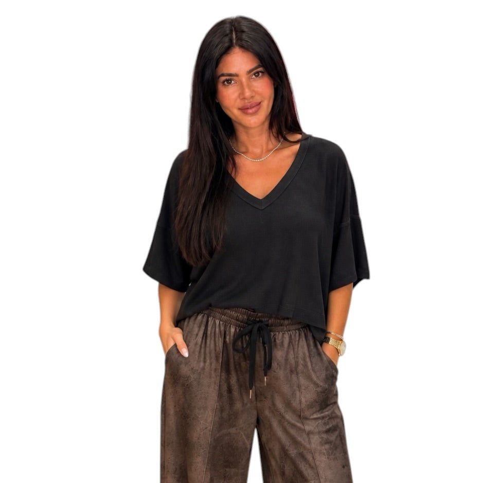 A woman modeling a black short-sleeve V-neck top with brown textured drawstring pants against a plain white background.