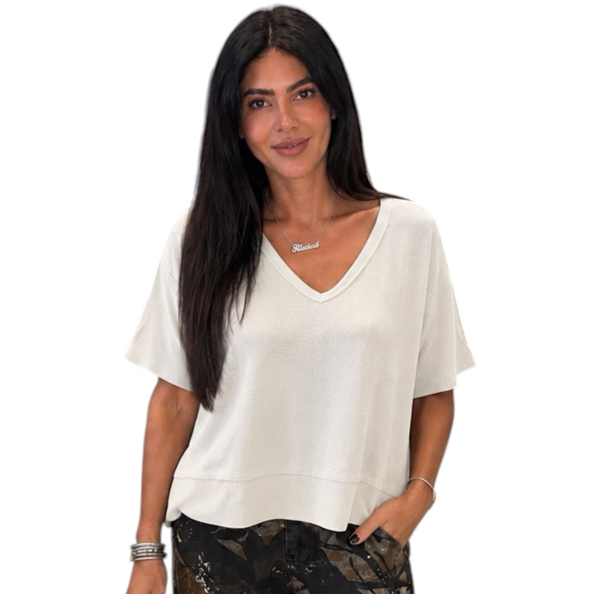 A woman modeling a short-sleeve V-neck top in off-white, paired with camouflage pants, against a plain white background.