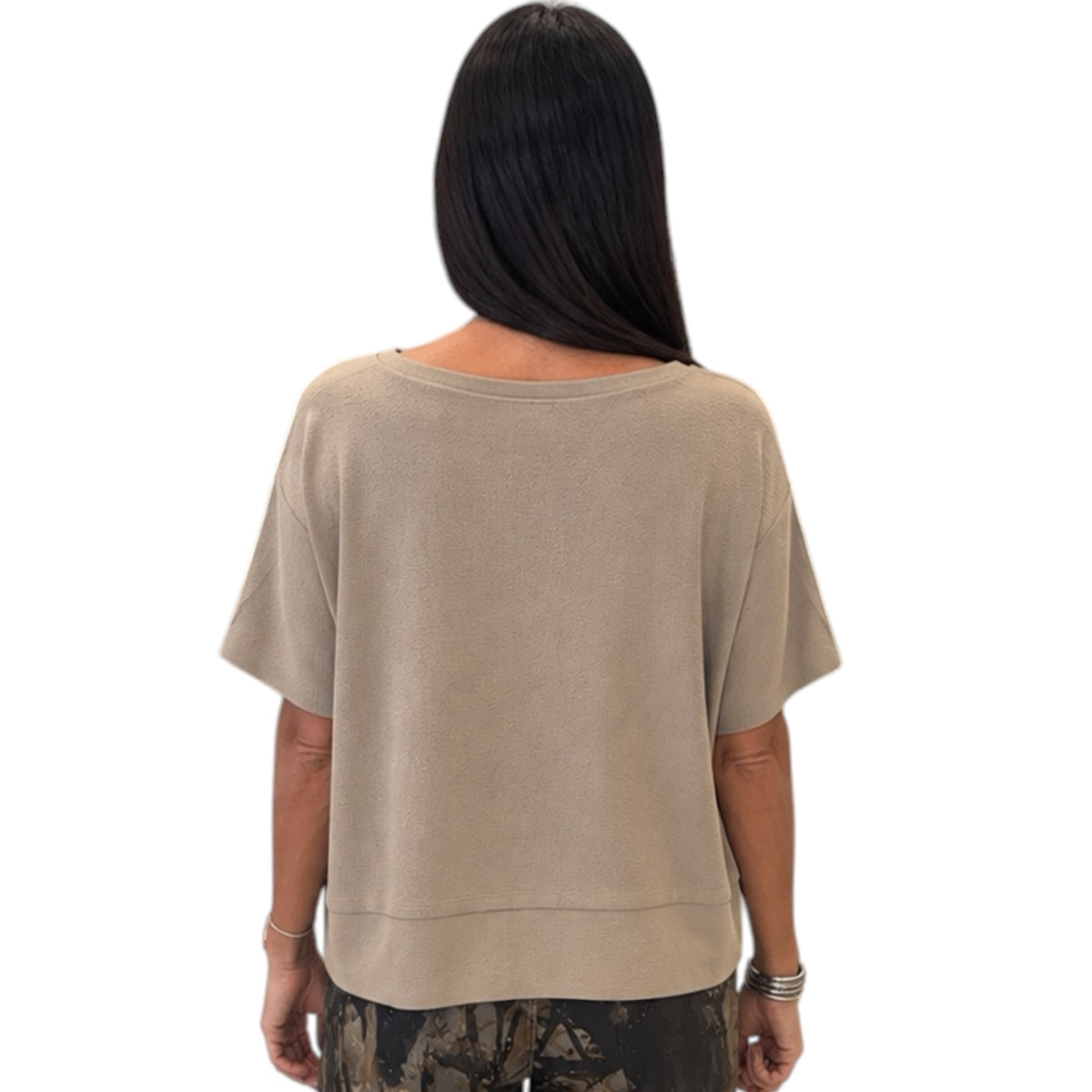 A woman viewed from the back wearing a loose, short-sleeve beige top and camouflage-patterned pants against a plain white background.