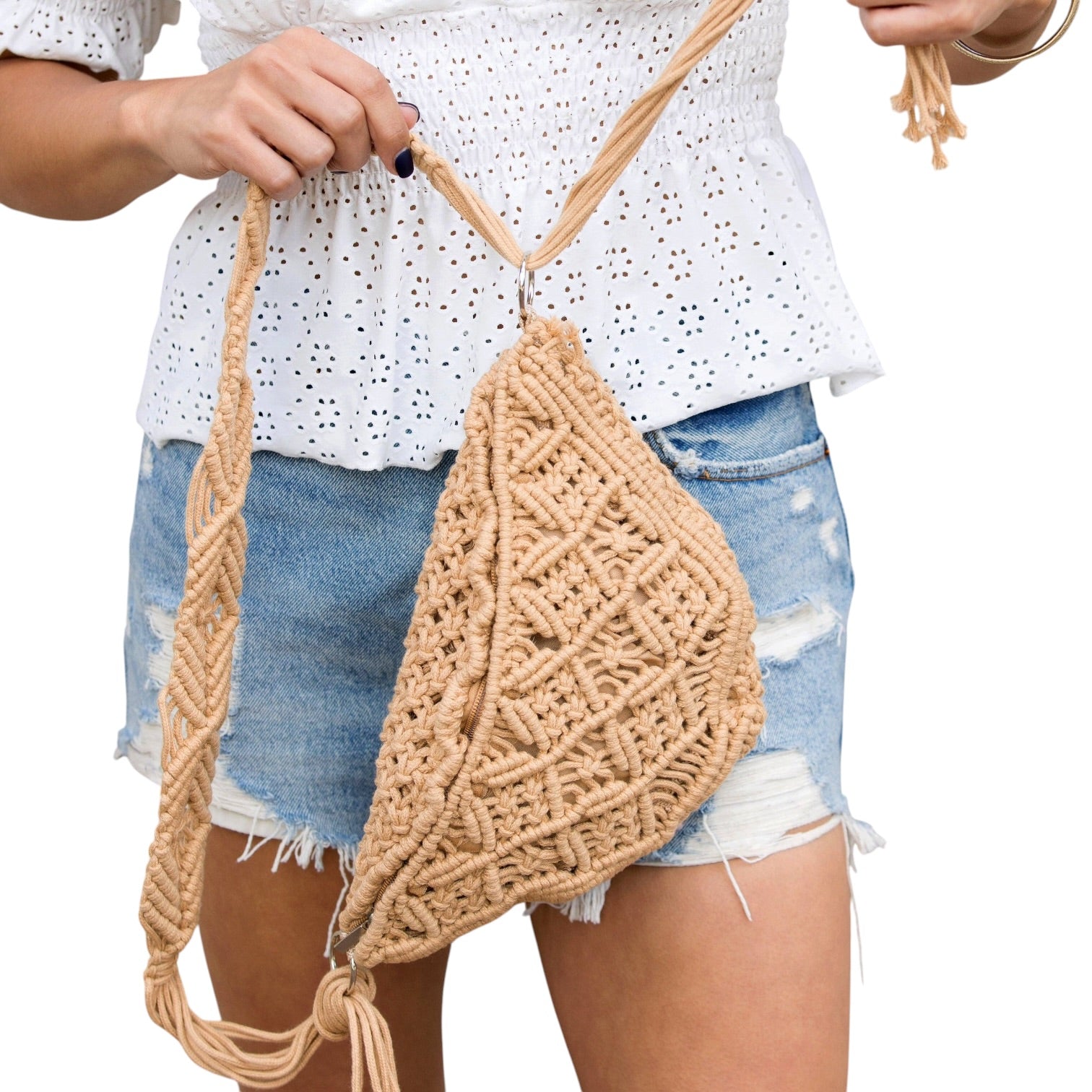 Person holding a woven beige bag with a white top and denim shorts on a plain background