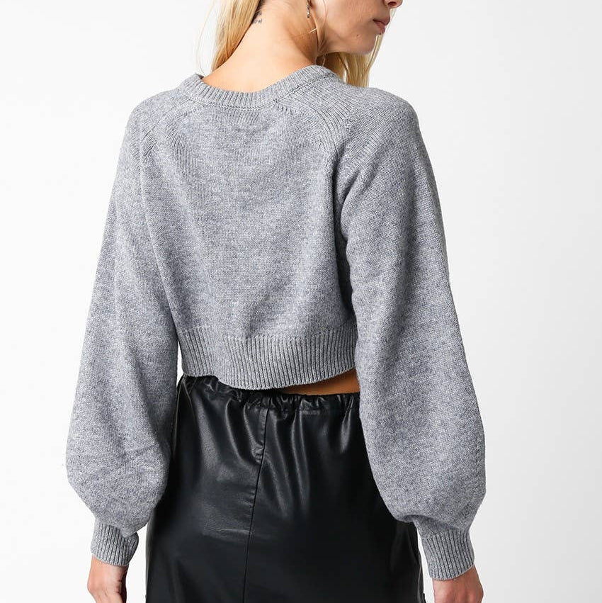 Person wearing a gray sweater and black pants on a white background