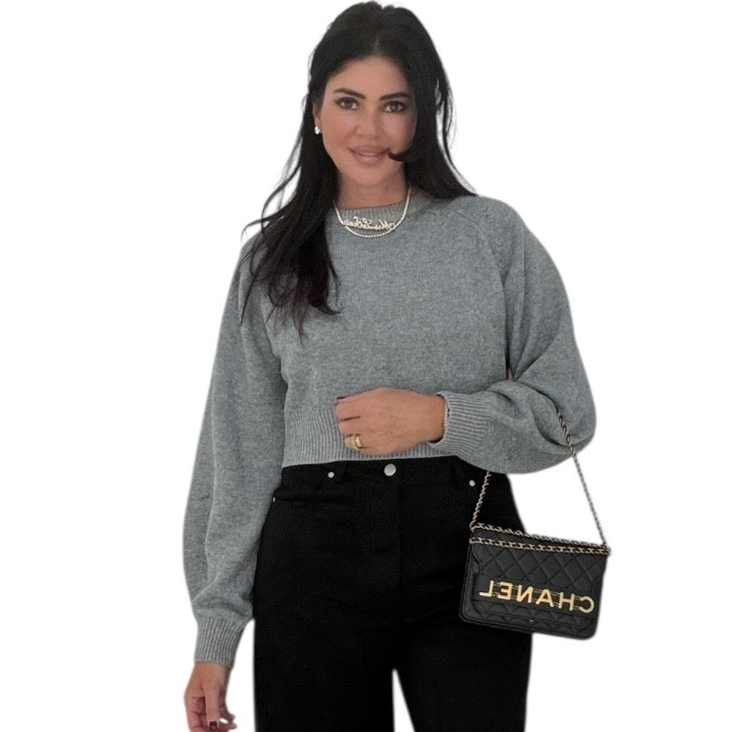 Woman wearing a gray sweater and black pants holding a black handbag with 'Chanel' branding.