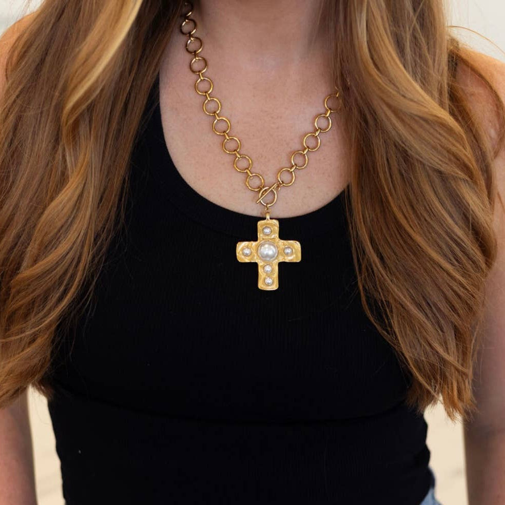 Gold chain necklace with a cross pendant worn by a person with long hair.
