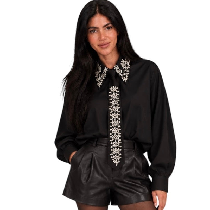 A woman modeling a black long-sleeve blouse with ornate silver beaded embroidery on the collar and front placket, paired with black shorts, against a plain white background.