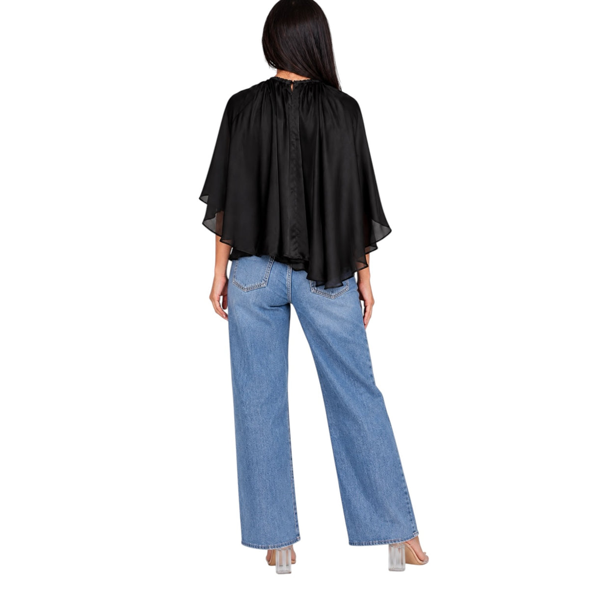 A woman shown from the back wearing a black sheer cape-style blouse with wide draped sleeves and light blue wide-leg jeans, against a plain white background.