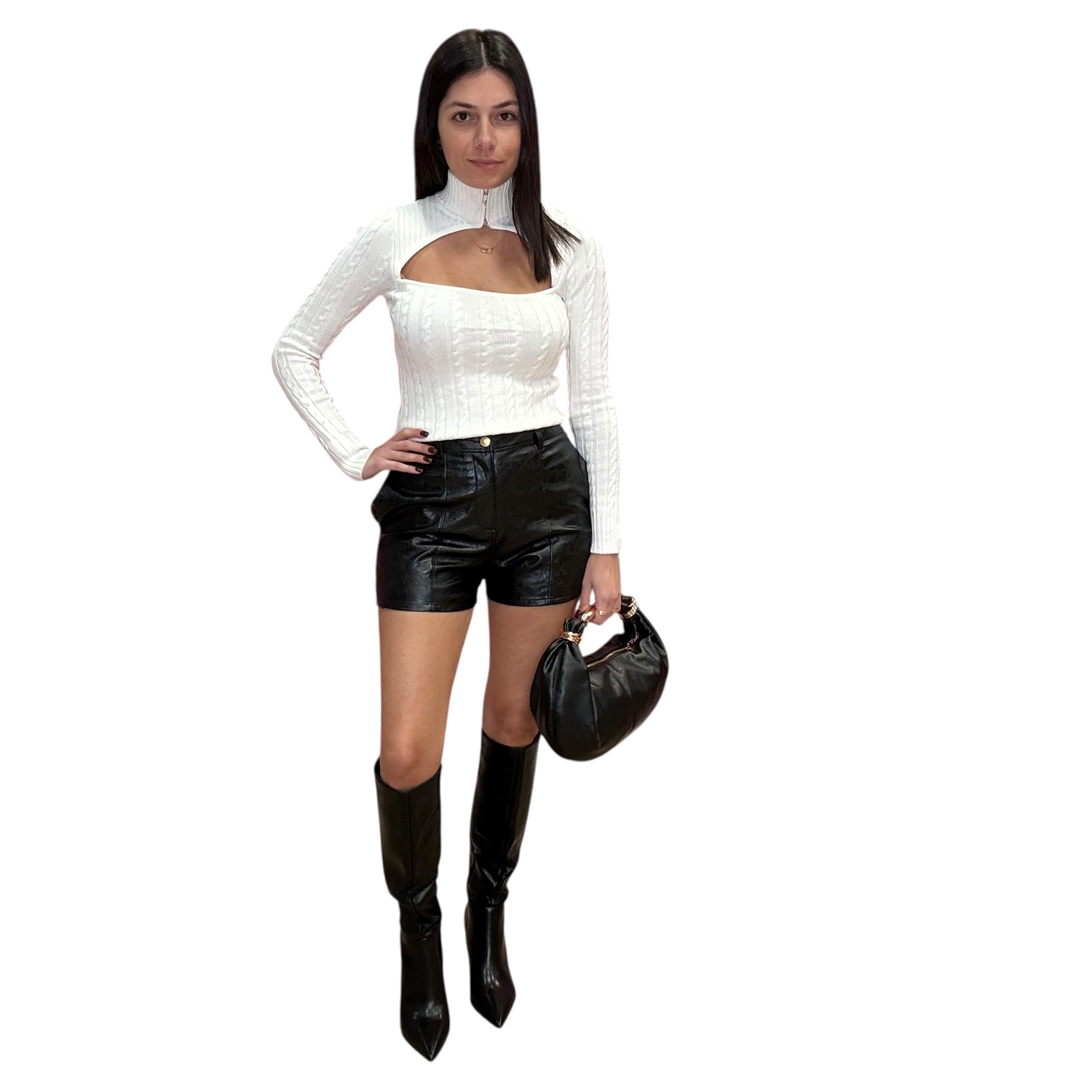 Woman wearing a white long-sleeve sweater and black leather shorts with black knee-high boots on a white background.