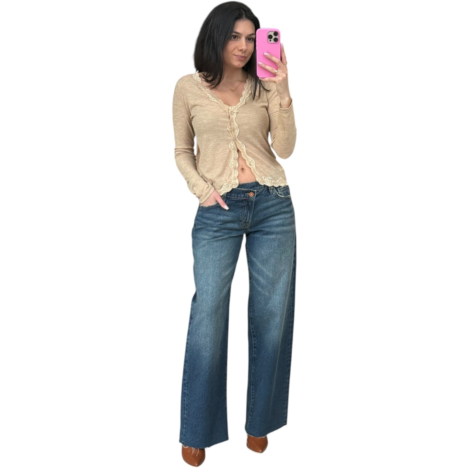 Woman taking a selfie wearing a beige cardigan and blue jeans on a white background