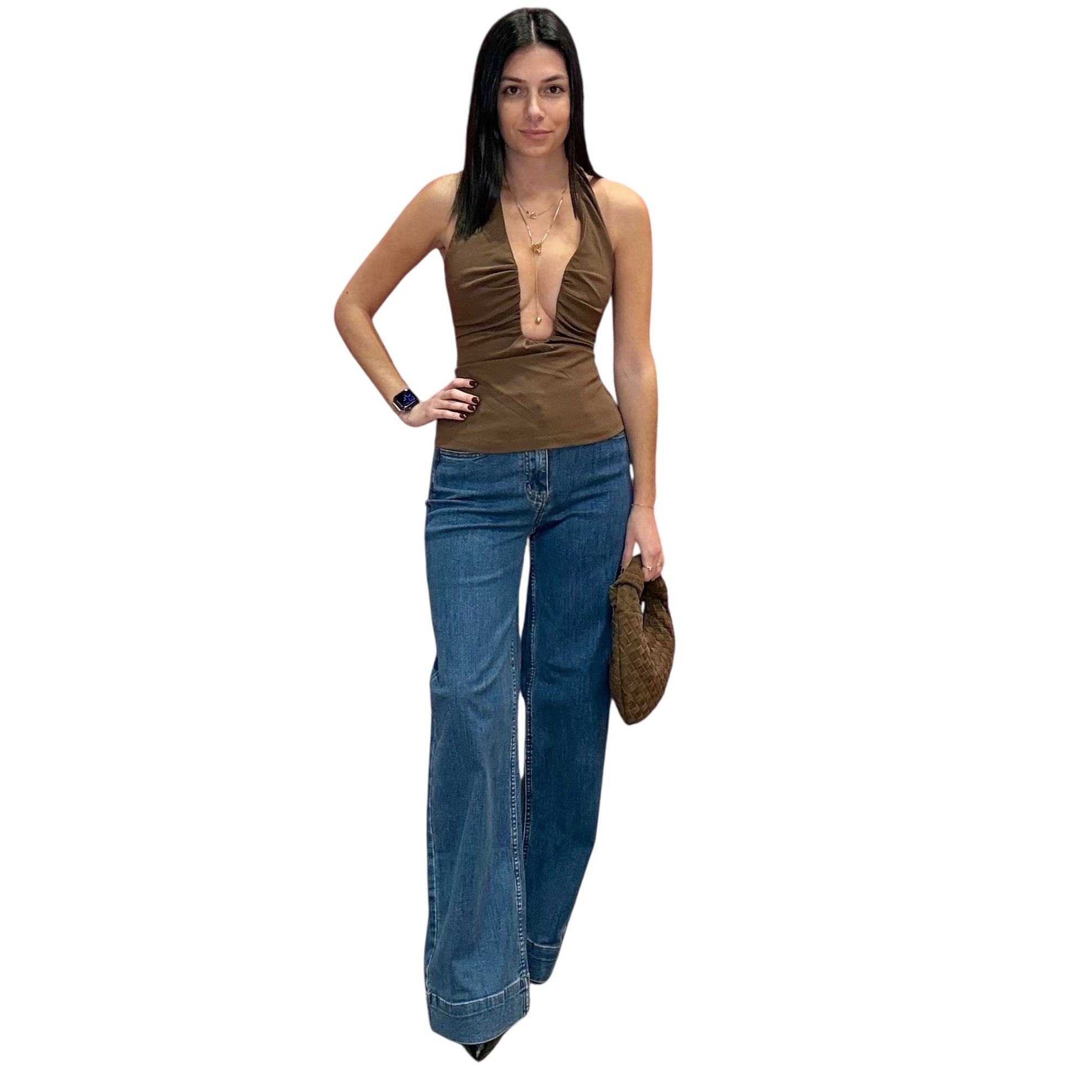 Woman wearing a brown top and blue jeans holding a handbag on a white background