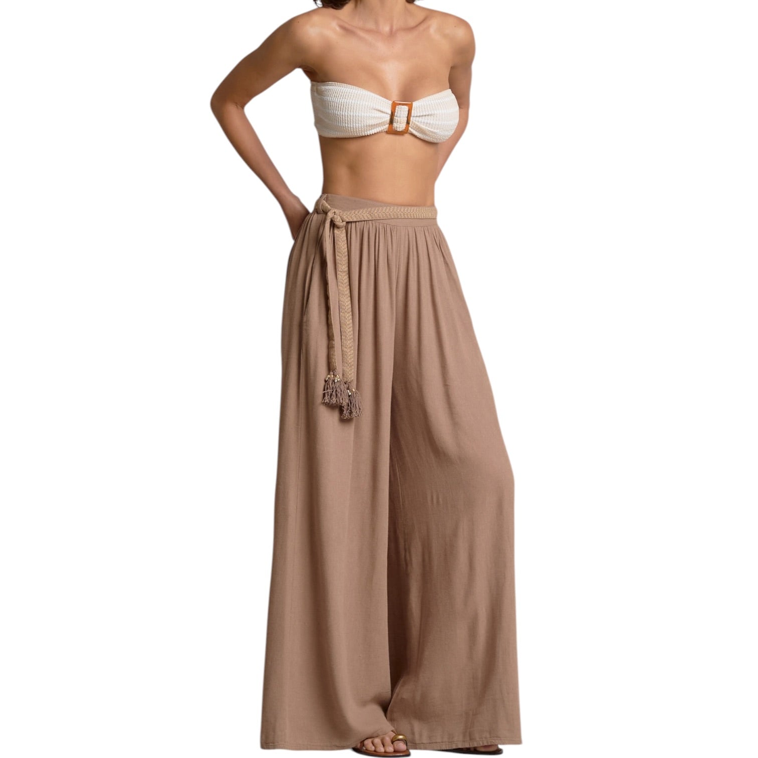 Woman wearing a white strapless top and brown flowing pants on a white background