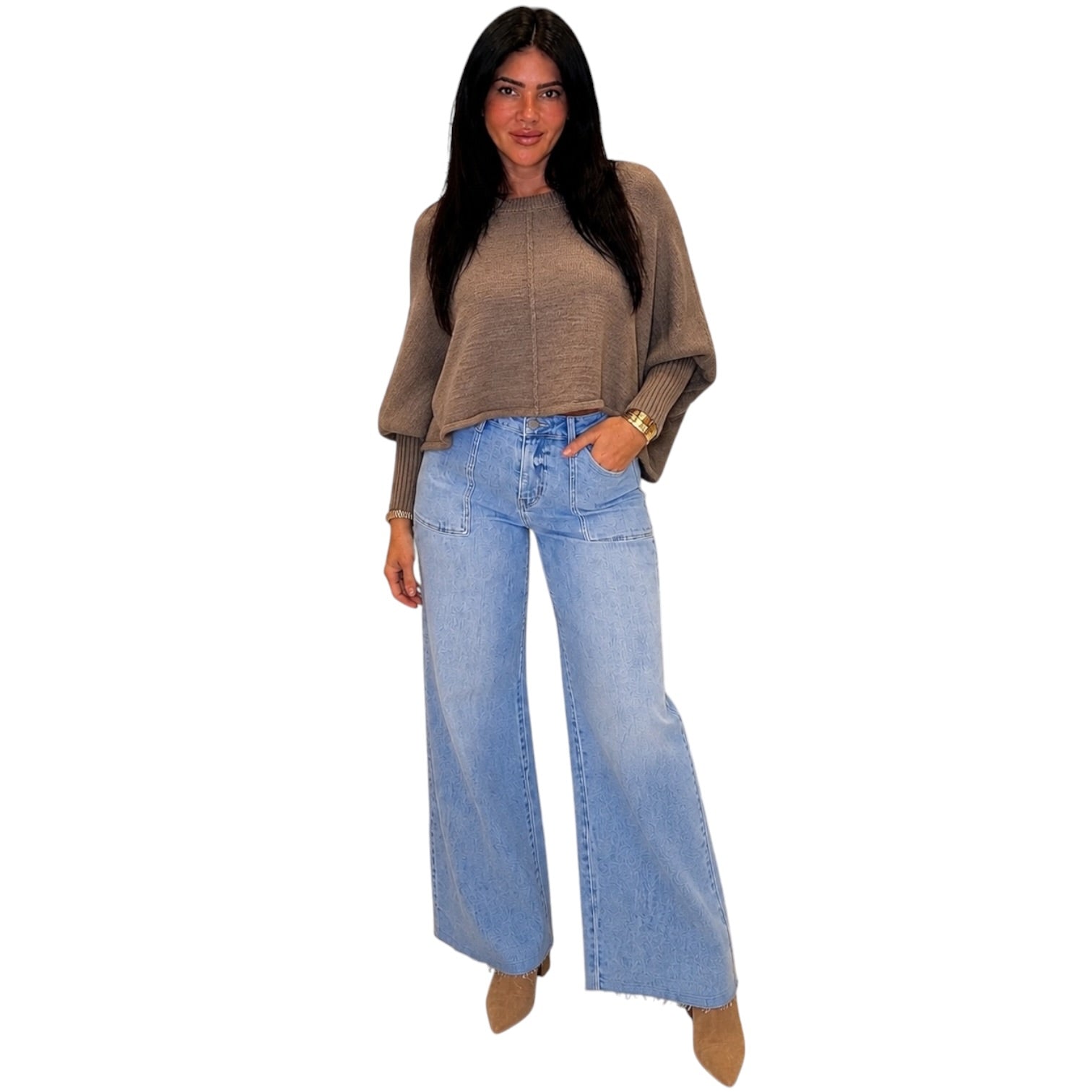 A woman modeling a cropped taupe knit sweater with wide batwing sleeves and light-wash blue wide-leg jeans, standing against a plain white background.