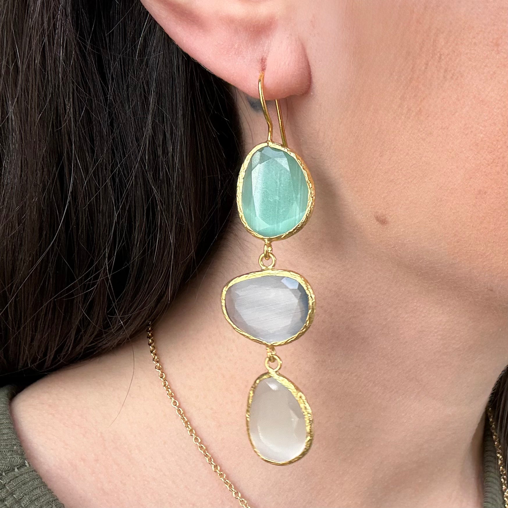 Close-up of a woman wearing gold earrings with green and white stones.