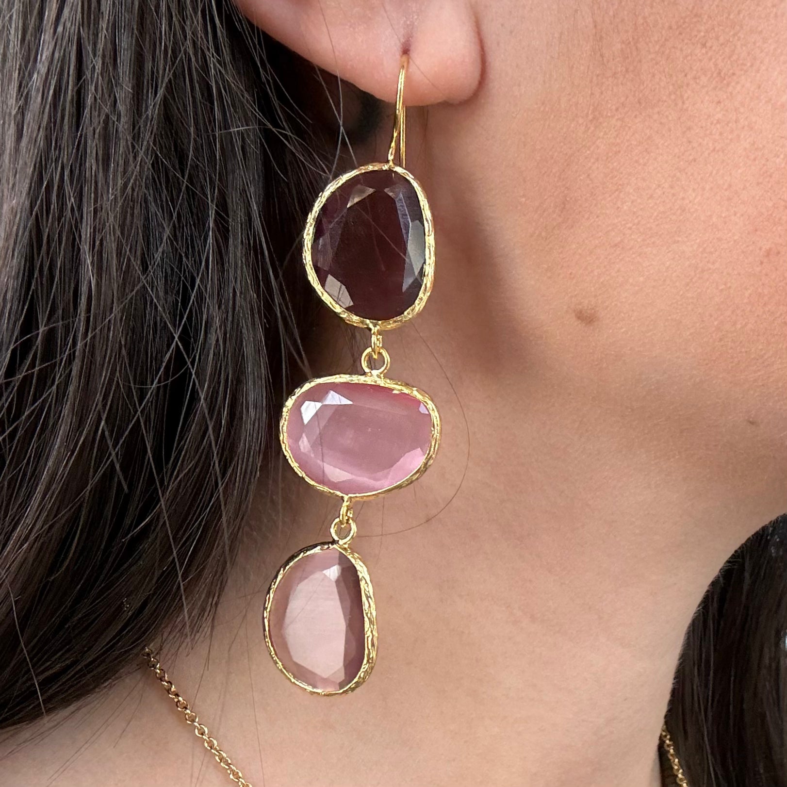 Gold earrings with multicolored stones worn by a person with dark hair.